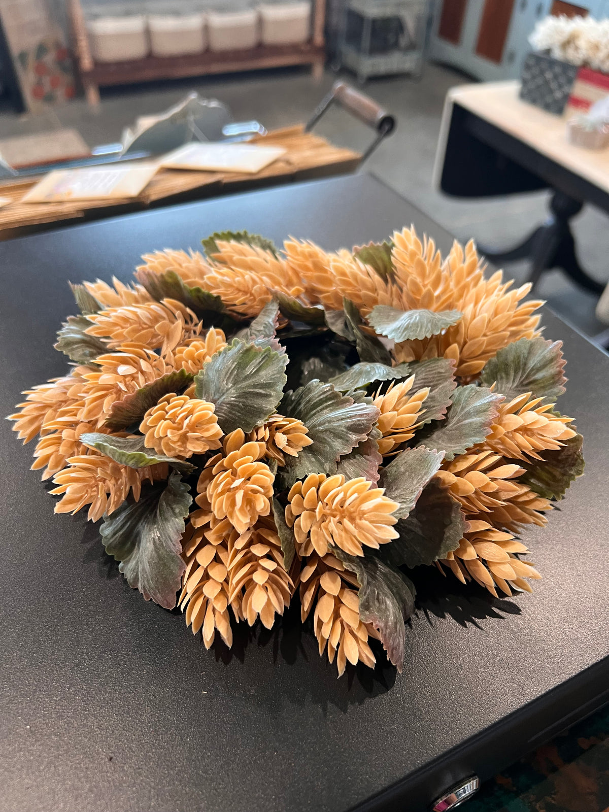 A decorative artificial floral wreath 
/candle ring with tan hops clusters and muted green leaves.