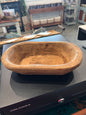 A rustic oval wooden bowl with a natural hand-hewn texture.
